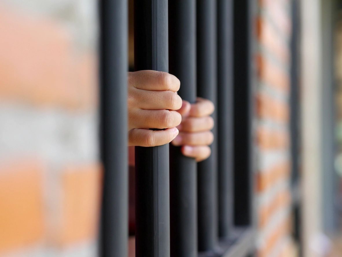 A person is holding onto bars of jail cell.